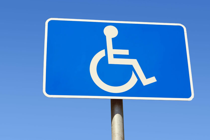 A blue and white International Symbol of Access sign against a bright blue sky.
