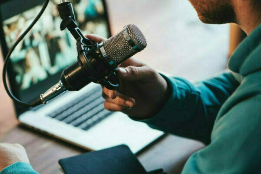 A person records a podcast using microphone and laptop.