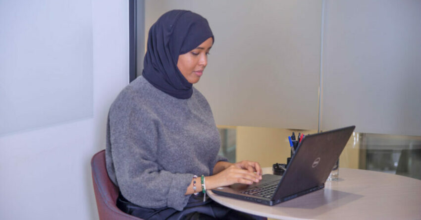 A hijab-wearing Black woman working on laptop
